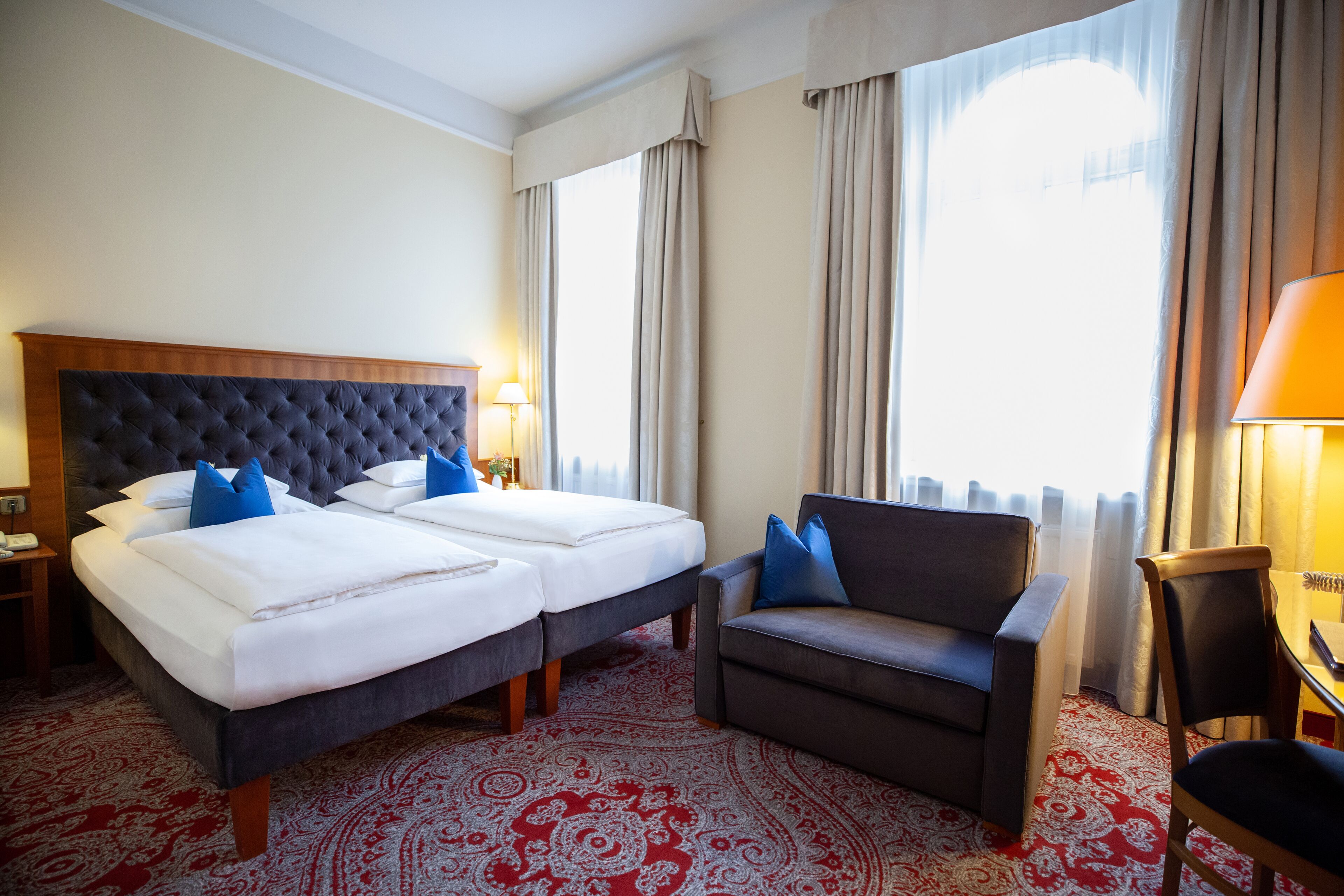 Una habitación de hotel con una cama grande, dos mesitas de noche, un sofá, una silla y un escritorio con una lámpara.