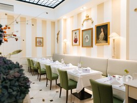 Um restaurante com paredes listradas, cadeiras estofadas em verde e toalhas de mesa brancas.