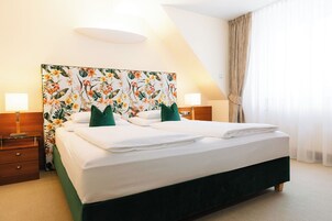 Una camera d'albergo con un letto grande, due comodini, una testiera fiorata e una finestra con tende.