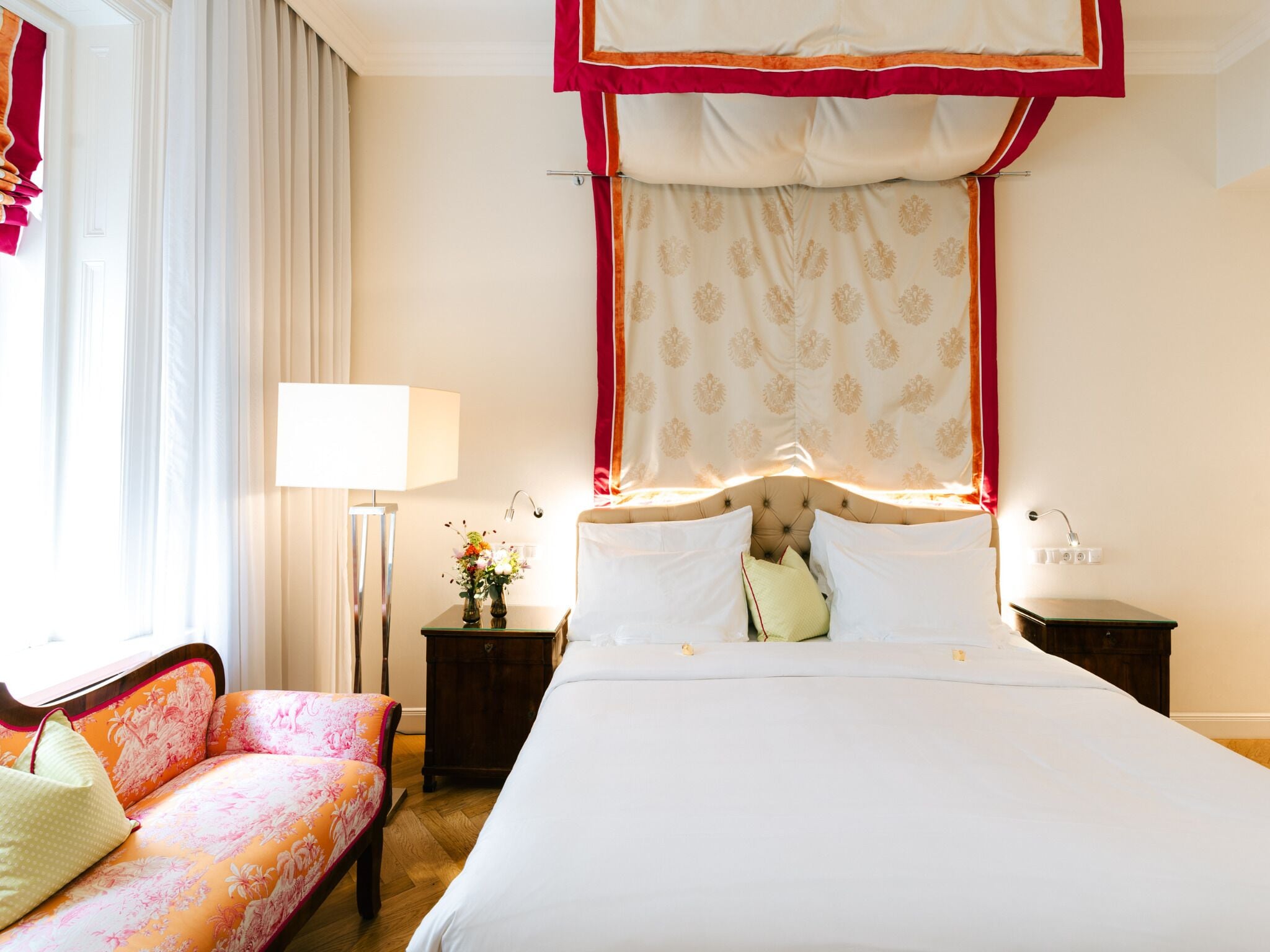 Habitación de hotel con una cama grande, un sofá, una mesita de noche con lámpara y una ventana con cortinas.