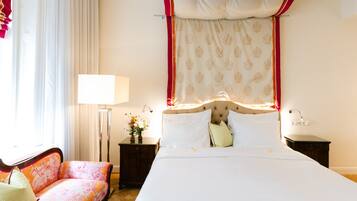 Habitación de hotel con una cama grande, un sofá, una mesita de noche con lámpara y una ventana con cortinas.