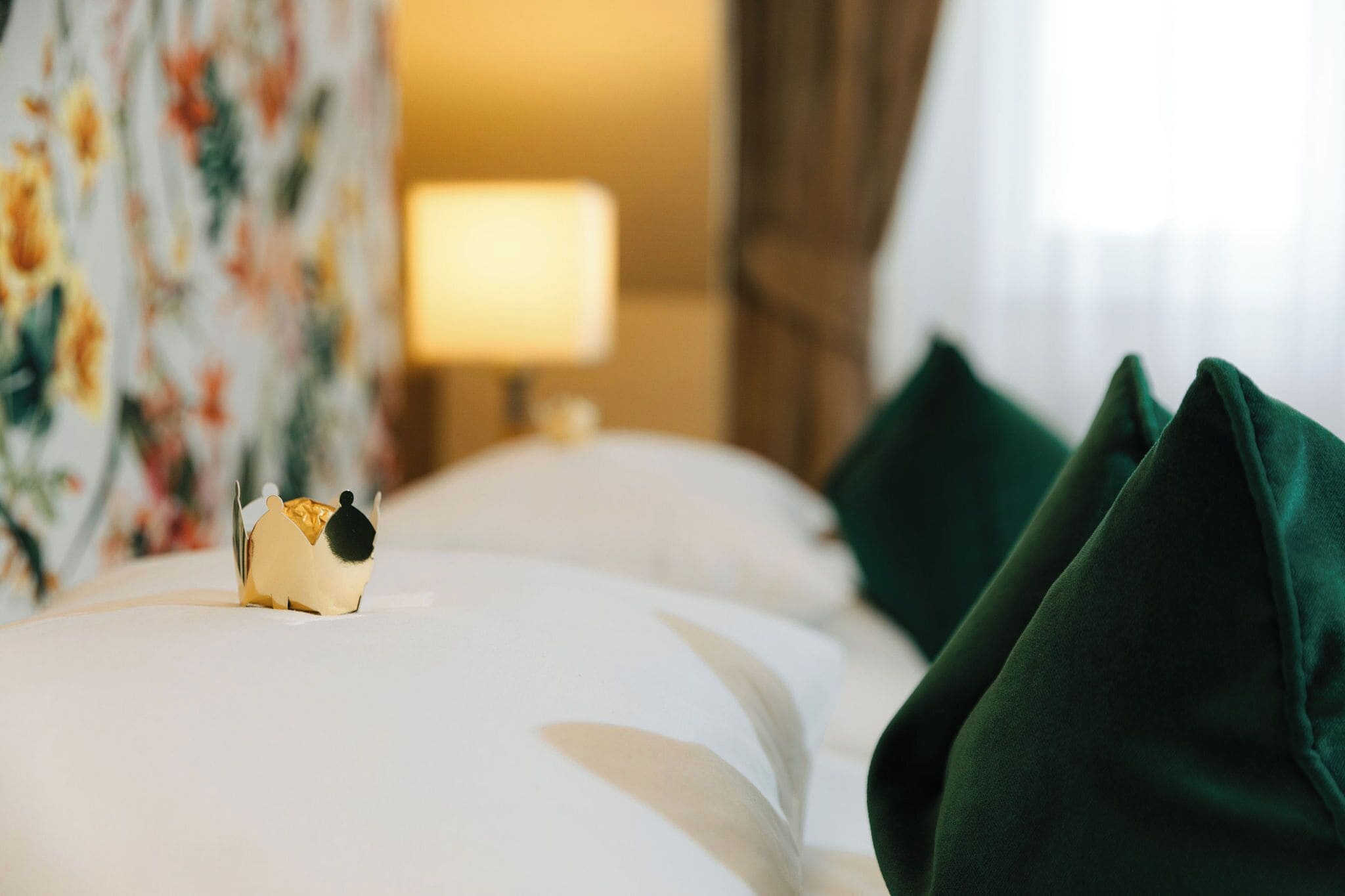 A neatly made bed with a decorative object on the left side, a lamp in the background, and green pillows on the right.