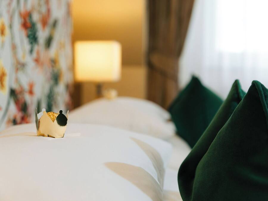 A neatly made bed with a decorative object on the left side, a lamp in the background, and green pillows on the right.