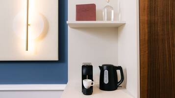 A coffee maker, a cup, a book, and a bottle on a shelf.