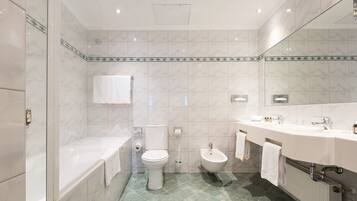 Een moderne badkamer met een bad, toilet, bidet en een grote spiegel.