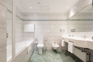 Een moderne badkamer met een bad, toilet, bidet en een grote spiegel.