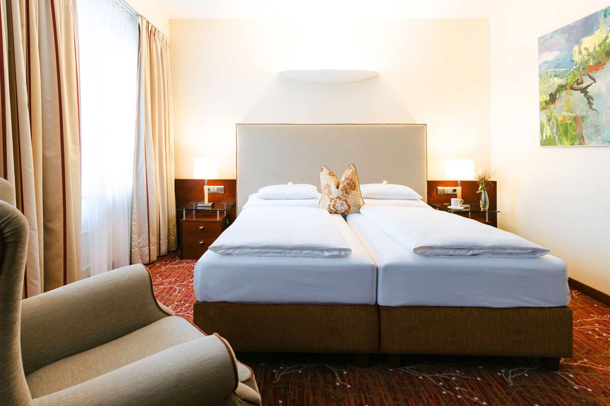 A hotel room with a double bed, two bedside tables with lamps, a chair, and a painting on the wall.