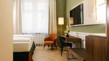 A hotel room with a bed, a desk with a lamp, a chair, and a TV mounted on the wall.