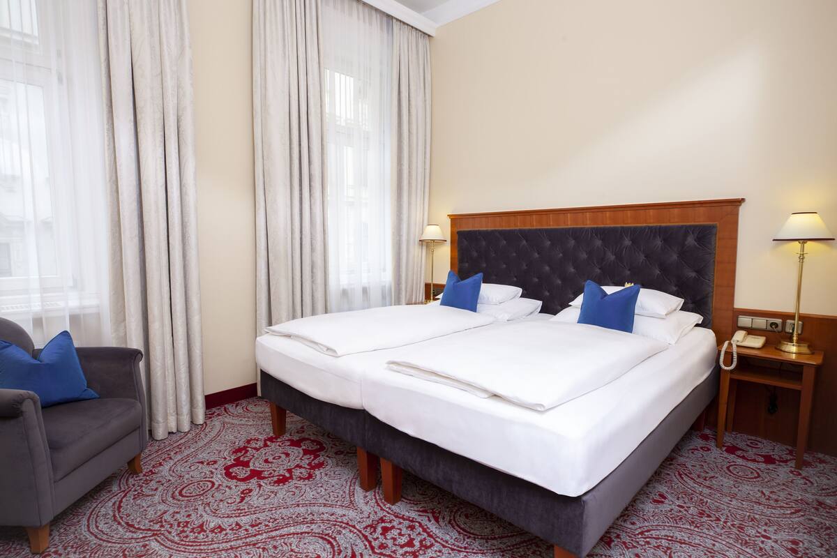 A hotel room with a large bed, two bedside tables, a chair, and a patterned carpet.