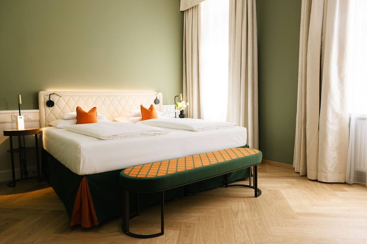 A neatly made bed with pillows, a bedside table with a lamp, and a bench at the foot of the bed.