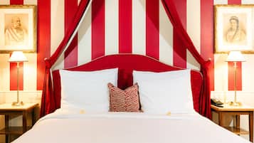 Una cama con sábanas blancas, cortinas a rayas rojas y blancas, y dos retratos enmarcados a cada lado.