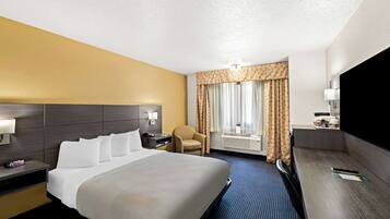 A hotel room with a large bed, a chair, a desk, and a TV.