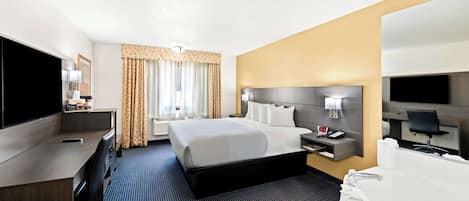 A hotel room with a large bed, a desk with a flat-screen TV, a bedside table with a lamp, and a bathroom with a bathtub and toilet.