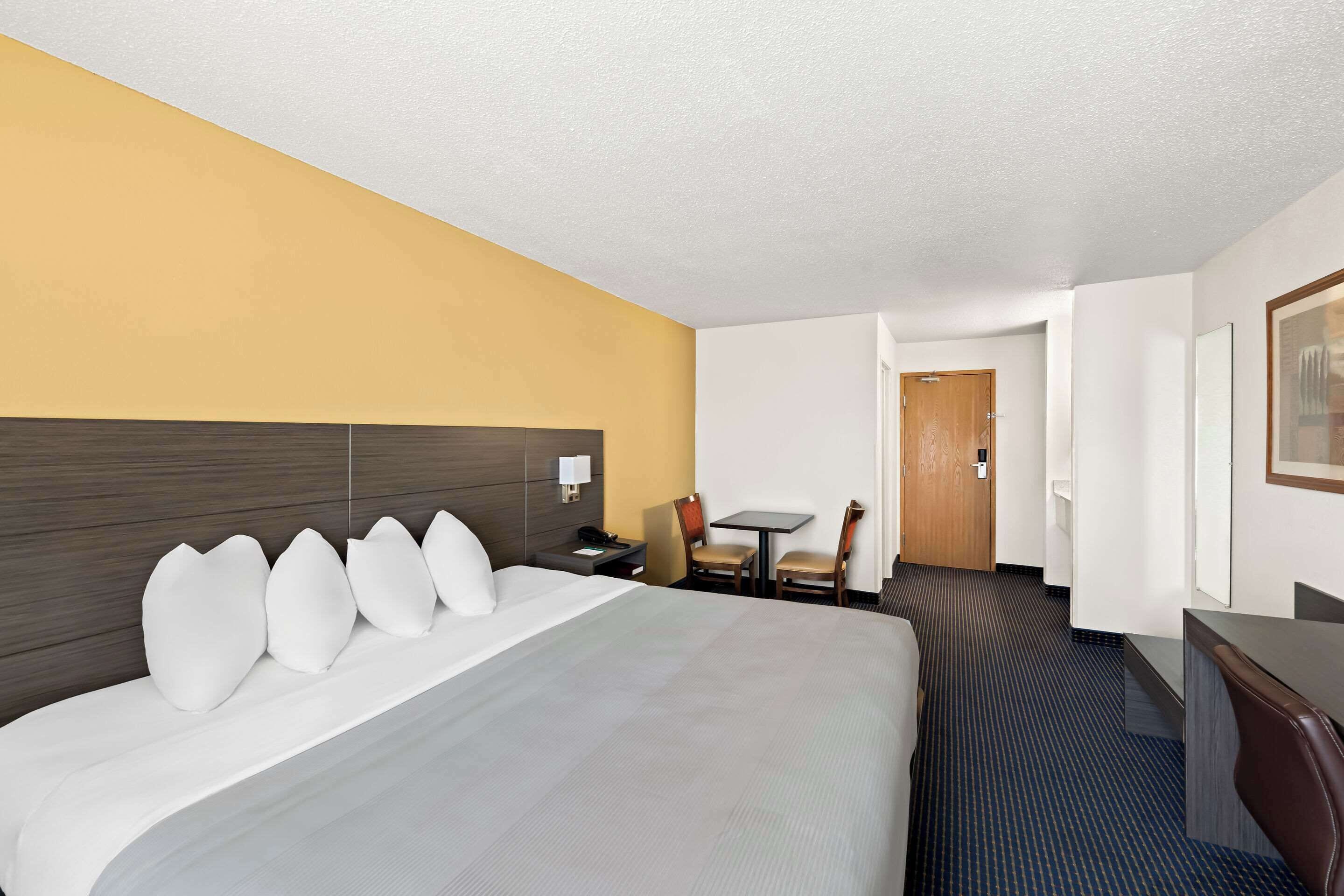 A hotel room with a large bed, a desk, a chair, and a small table.