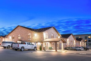 A brick building with multiple units, a covered parking area, and a few vehicles parked in front. - Quality Inn North Platte (North Platte)