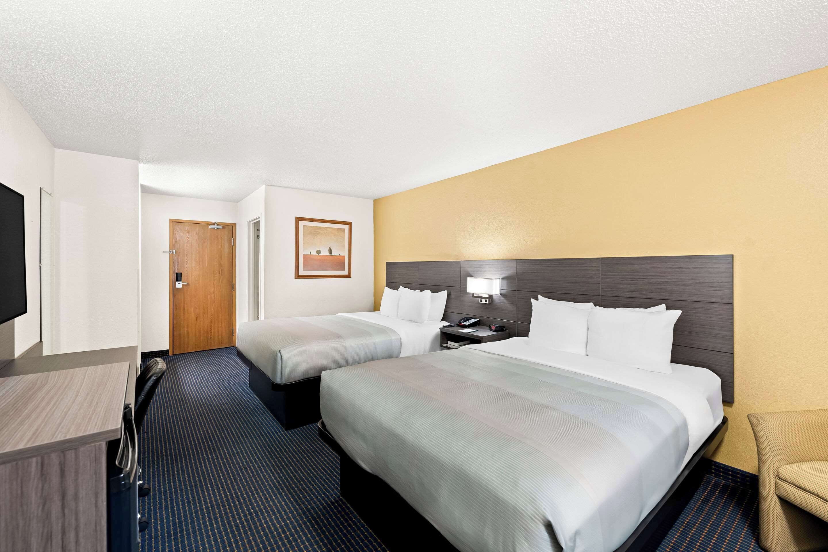A hotel room with two beds, a desk, a TV, and a chair.