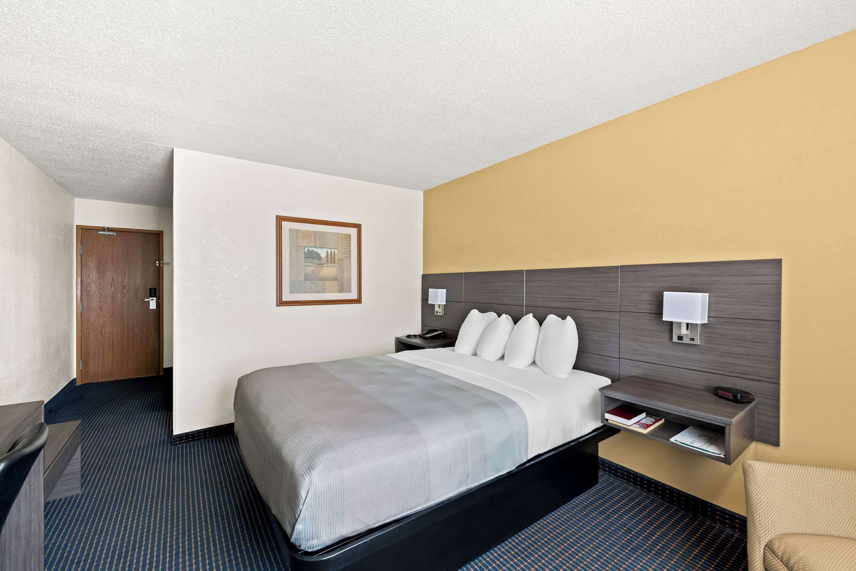 A hotel room with a bed, bedside table, lamp, and a door.