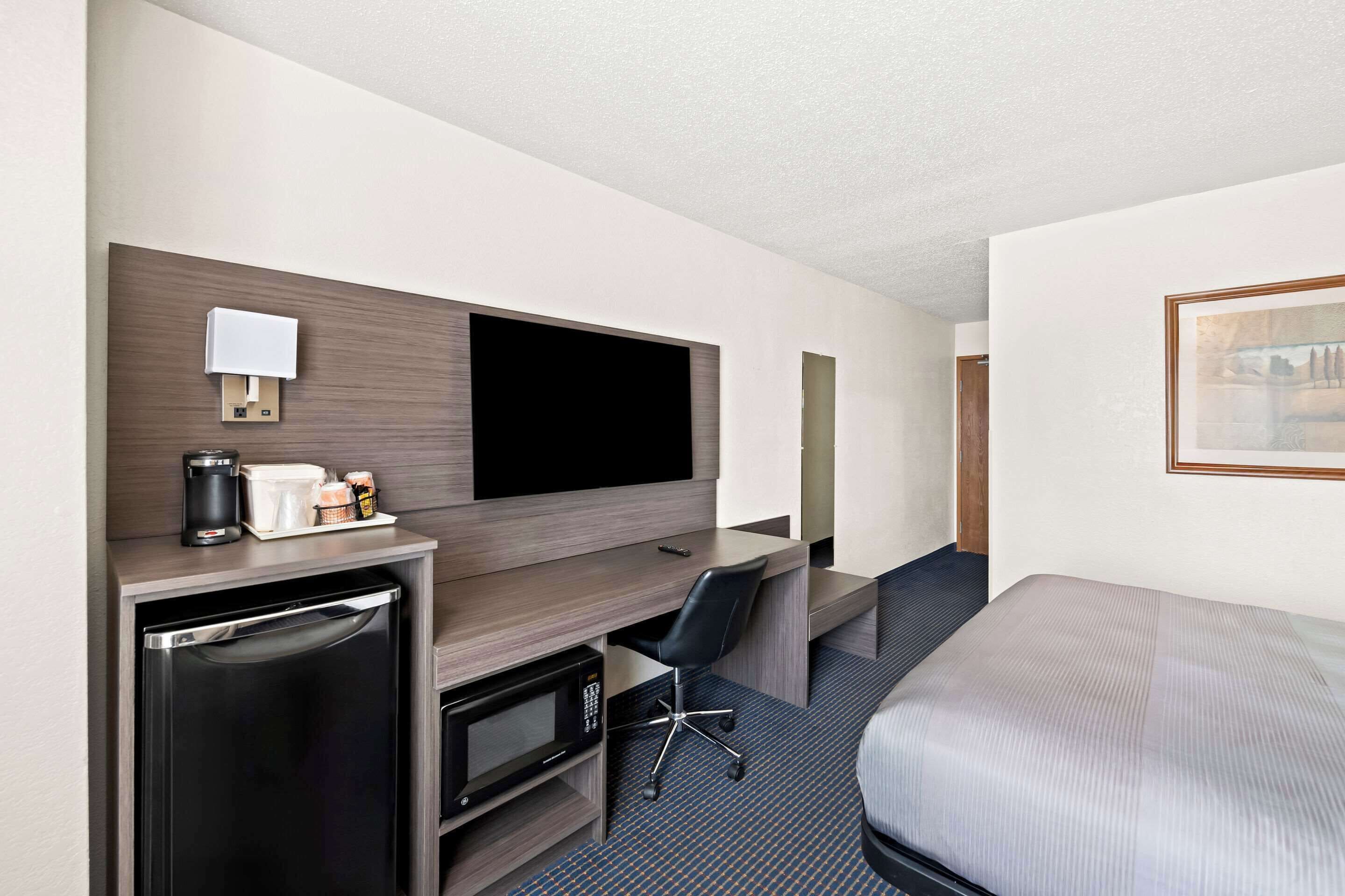 A hotel room with a bed, a desk with a computer, a microwave, a coffee maker, and a TV.