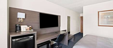 A hotel room with a bed, a desk with a computer, a microwave, a coffee maker, and a TV.