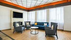 A modern living room with a stone accent wall, a flat-screen TV, a blue sofa, and two armchairs. - Comfort Inn & Suites Barrie - Highway 400 (Barrie)