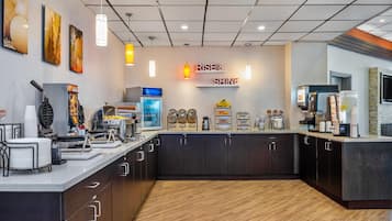 Una barra de desayuno moderna con un letrero que dice "RISE & SHINE", equipada con cafeteras, una presentación de frutas y diversas opciones para el desayuno.