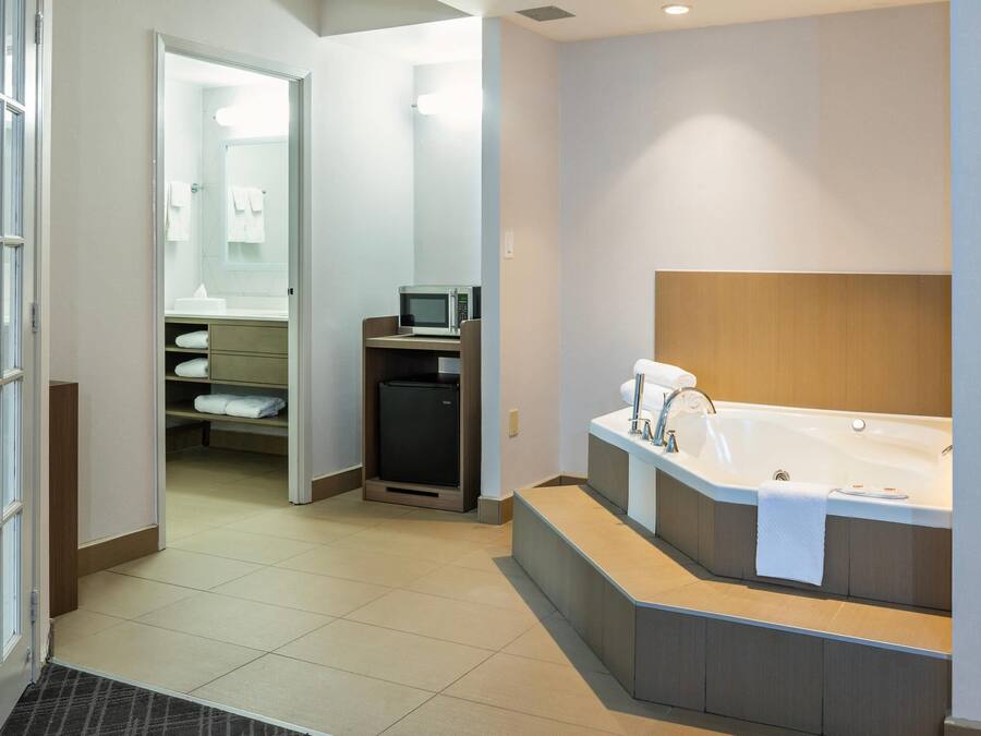 A modern bathroom with a large bathtub, a microwave, and a small refrigerator.