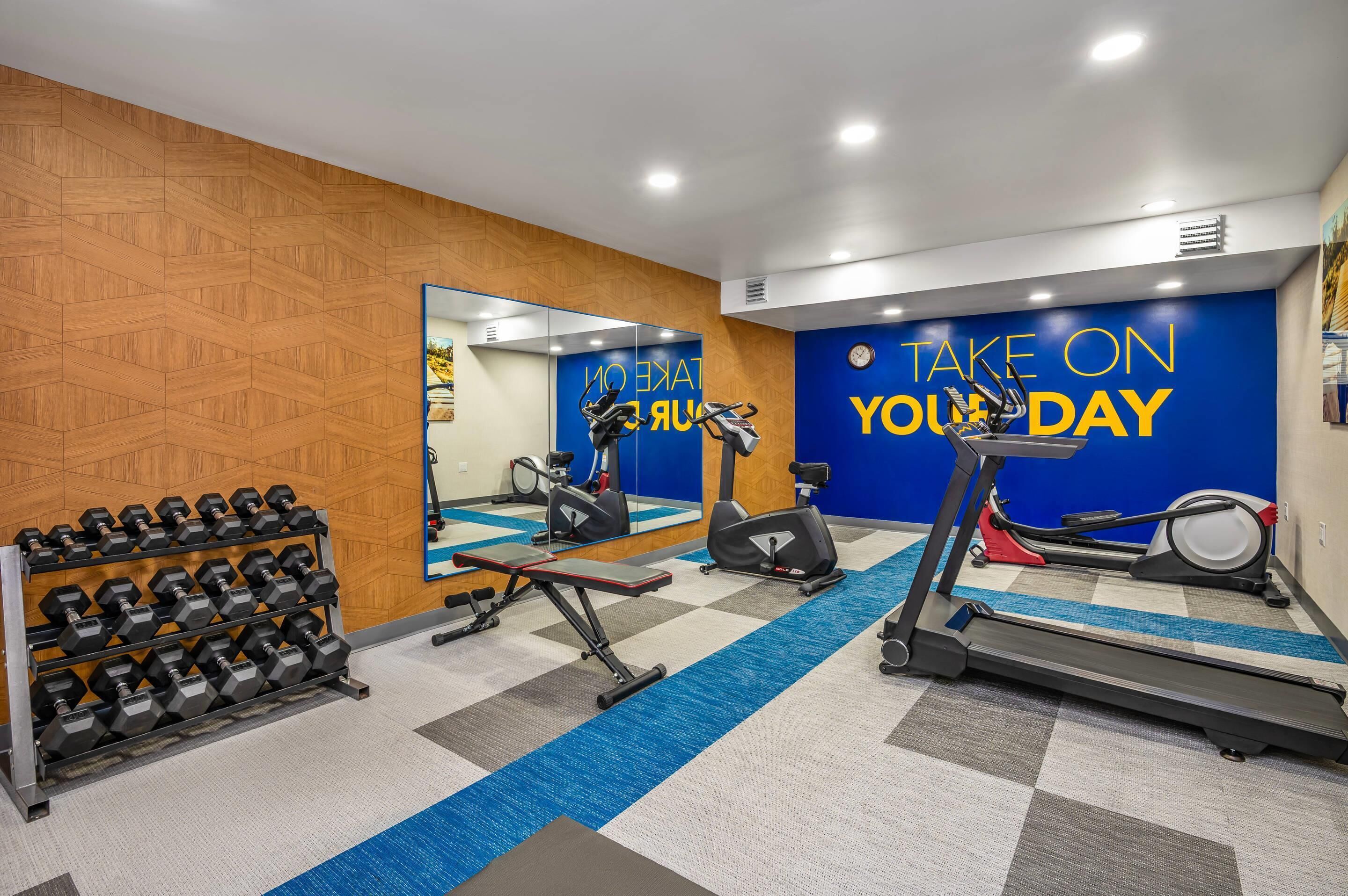 A gym with exercise equipment, a mirror, and motivational wall text.