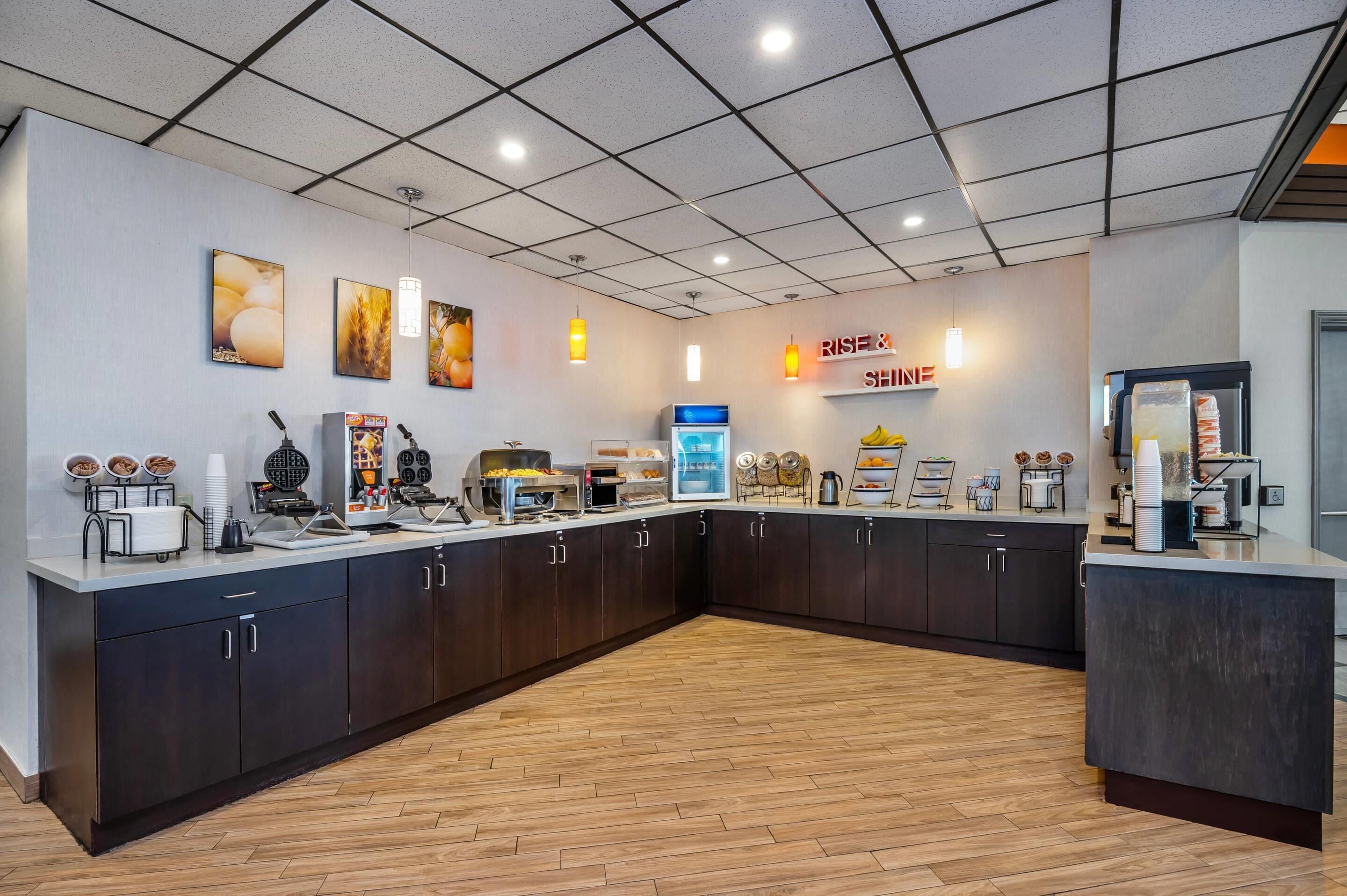 A modern kitchen area with a breakfast bar, coffee machines, and a sign that reads "RISE & Shine."