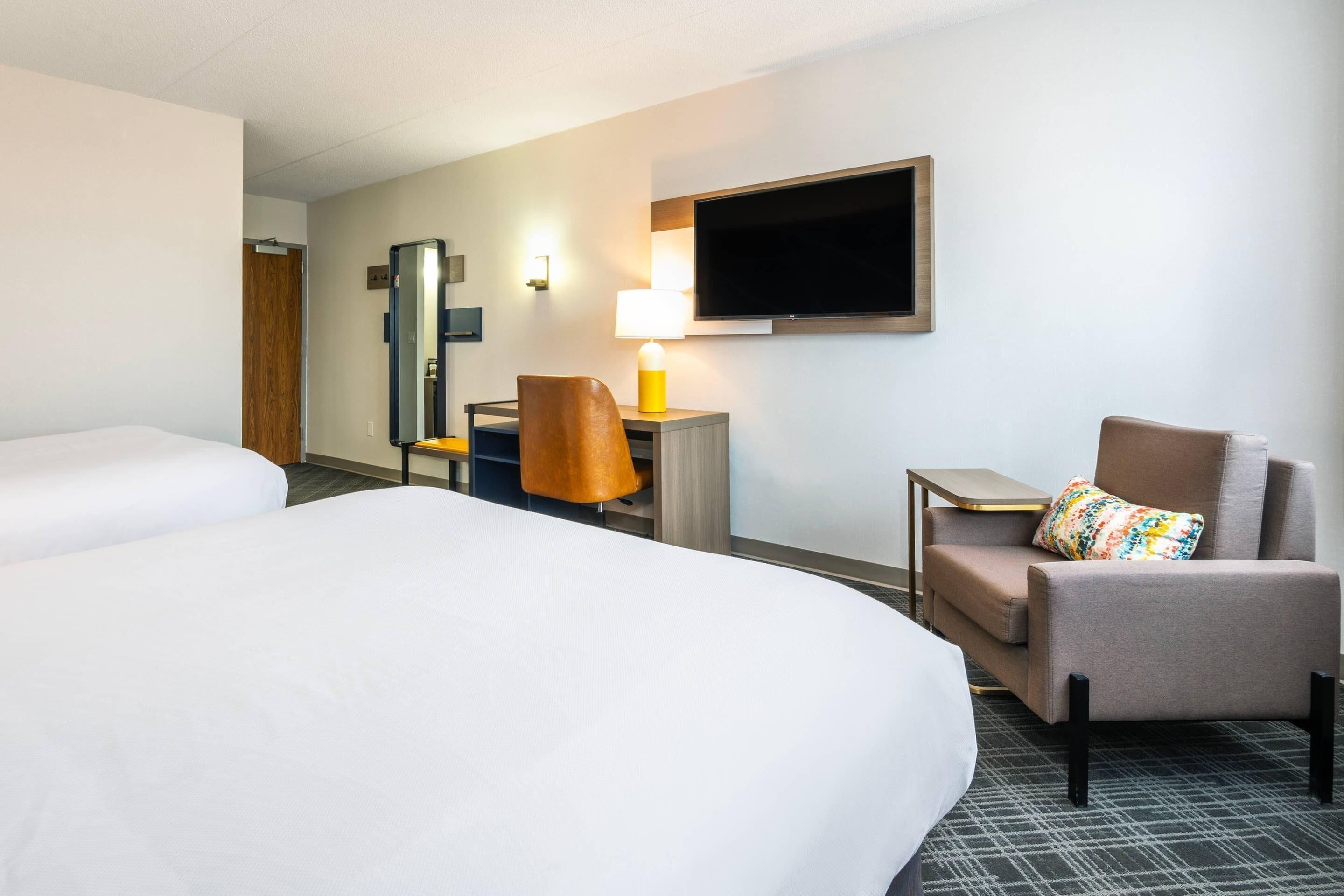 Een hotelkamer met twee bedden, een bureau met een lamp, een televisie en een stoel.