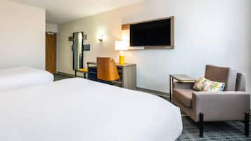 Een hotelkamer met twee bedden, een bureau met een lamp, een televisie en een stoel.