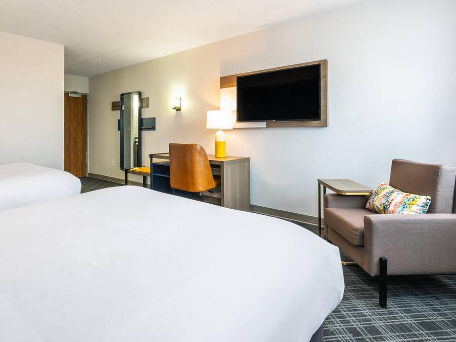 Een hotelkamer met twee bedden, een bureau met een lamp, een televisie en een stoel.