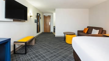 A hotel room with a bed, a sofa, a small table, a bench, and a TV mounted on the wall.