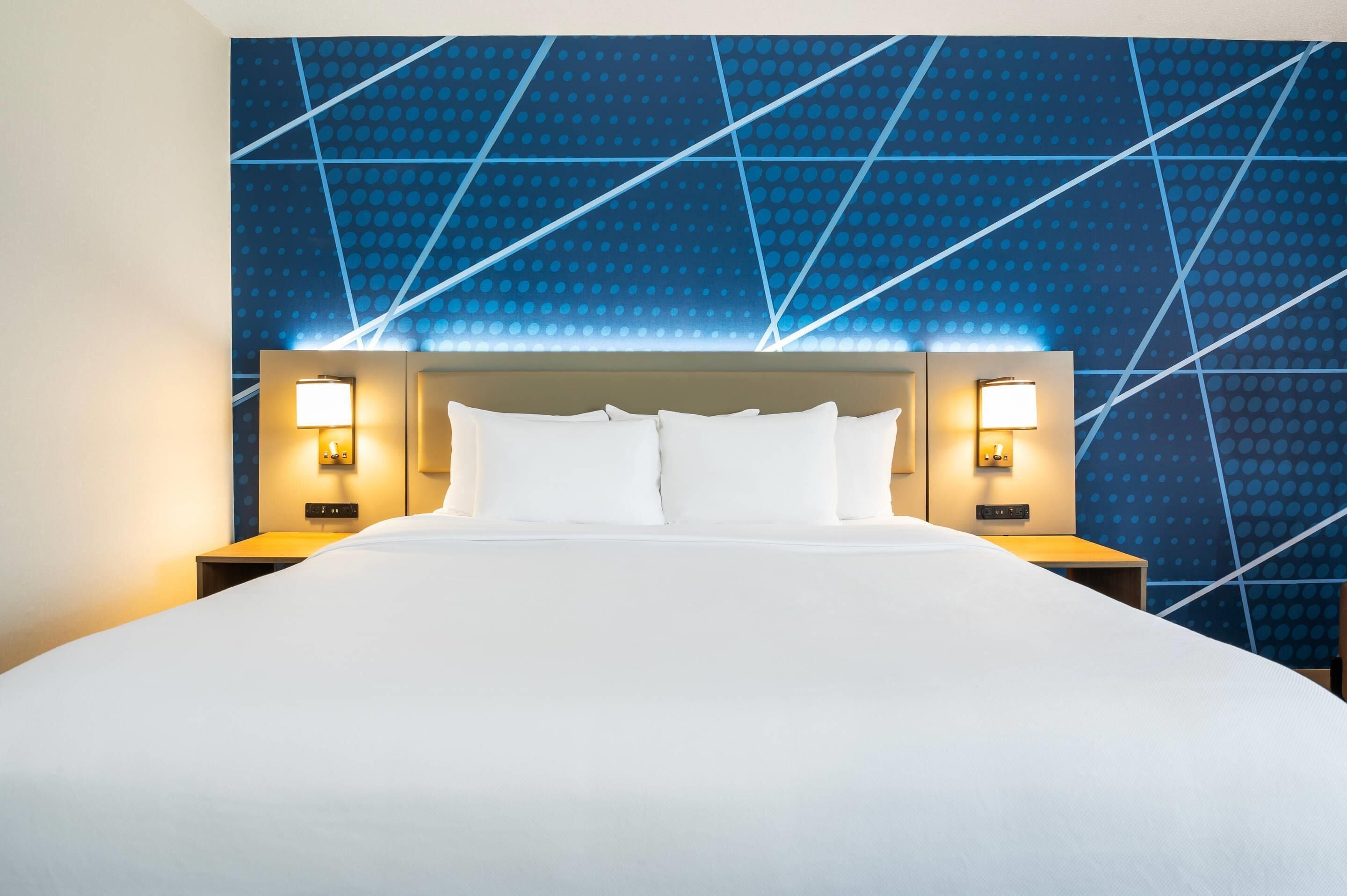 Una habitación de hotel con una cama grande, dos mesitas de noche con lámparas y una pared con diseño azulado.