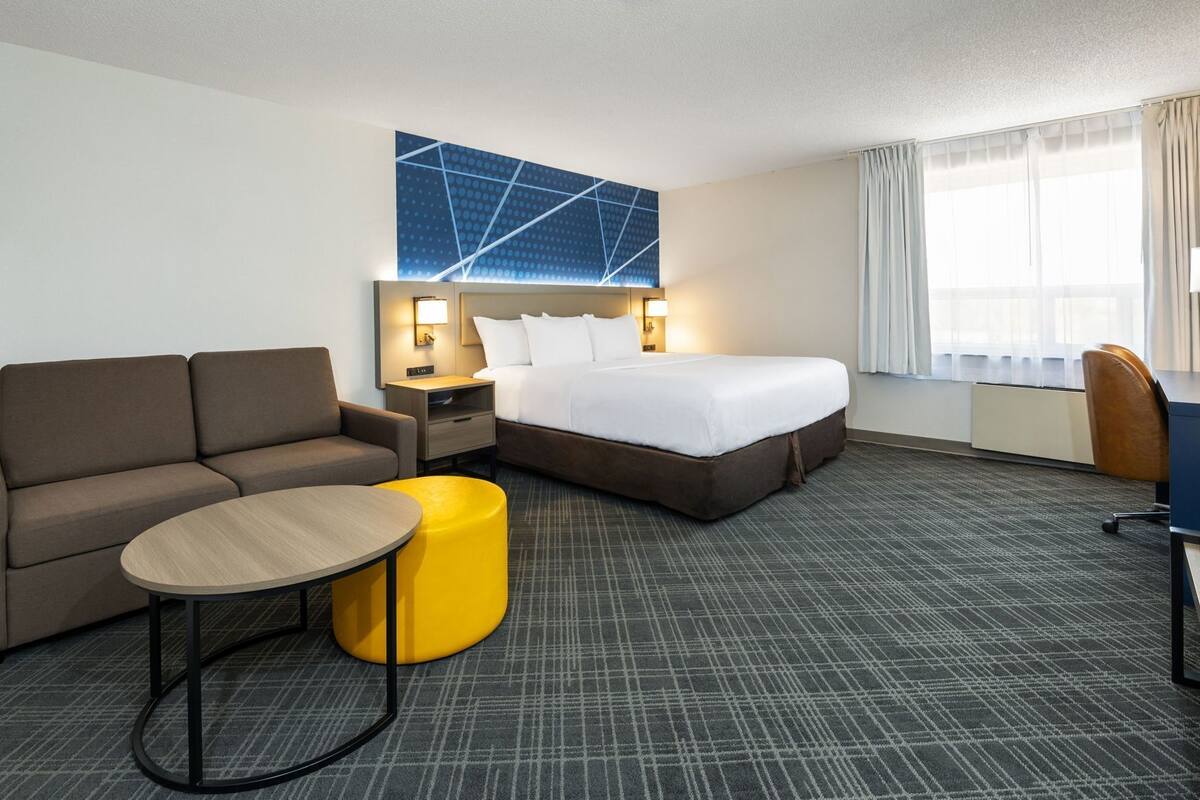 A hotel room with a bed, a sofa, a small table, a nightstand, and a desk.