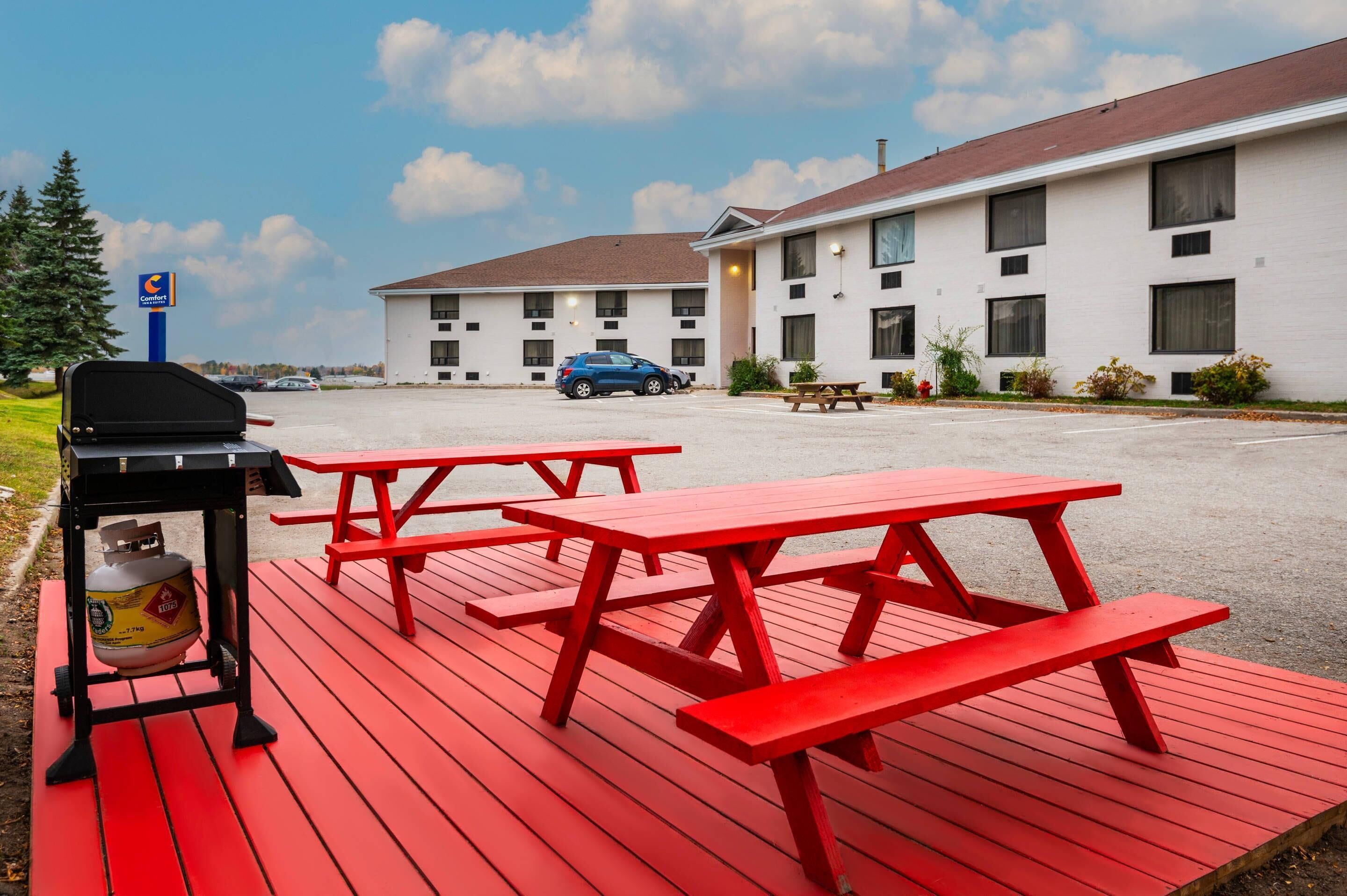 A motel with red picnic tables, a barbecue grill, and a parked car.