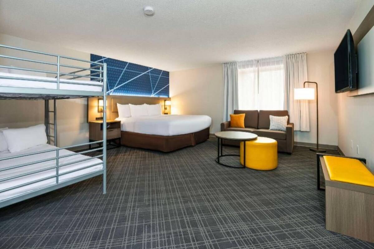 A hotel room with a bunk bed, a single bed, a sofa, a small table, and a TV.