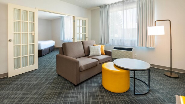 A hotel room with a sofa, a small round table, a lamp, and a bed in the background. - Comfort Inn & Suites Barrie - Highway 400 (Barrie)