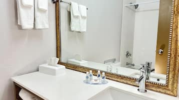 Ein Badezimmer mit einem weißen Waschbecken, einem großen Spiegel mit goldener Rahmung, einem Handtuchhalter mit weißen Handtüchern und einer im Hintergrund sichtbaren Toilette.
