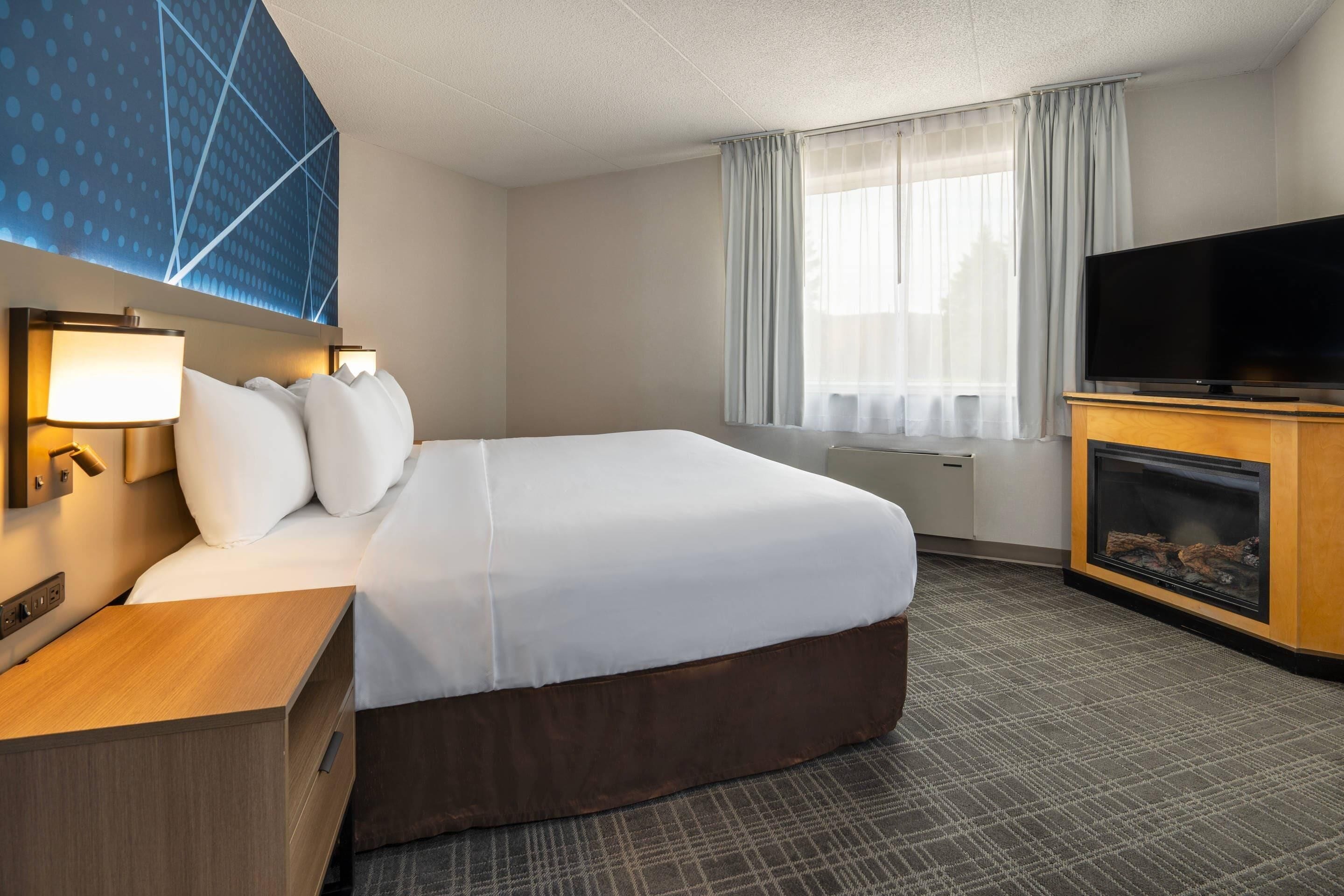 Une chambre d’hôtel avec un grand lit, un téléviseur à écran plat, une cheminée et une fenêtre avec des rideaux.