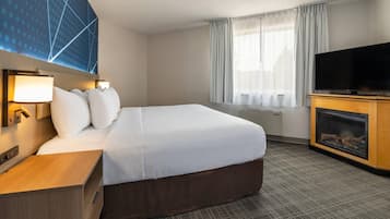 A hotel room with a large bed, a flat-screen TV, a fireplace, and a window with curtains.