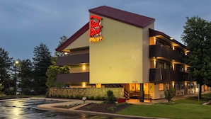 A multi-story hotel with a prominent 'Red Roof Plus' sign, a stone facade, and a landscaped front yard.
