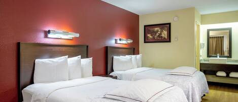 A hotel room with two beds, a red wall, a framed picture, and a bathroom visible through an open door.