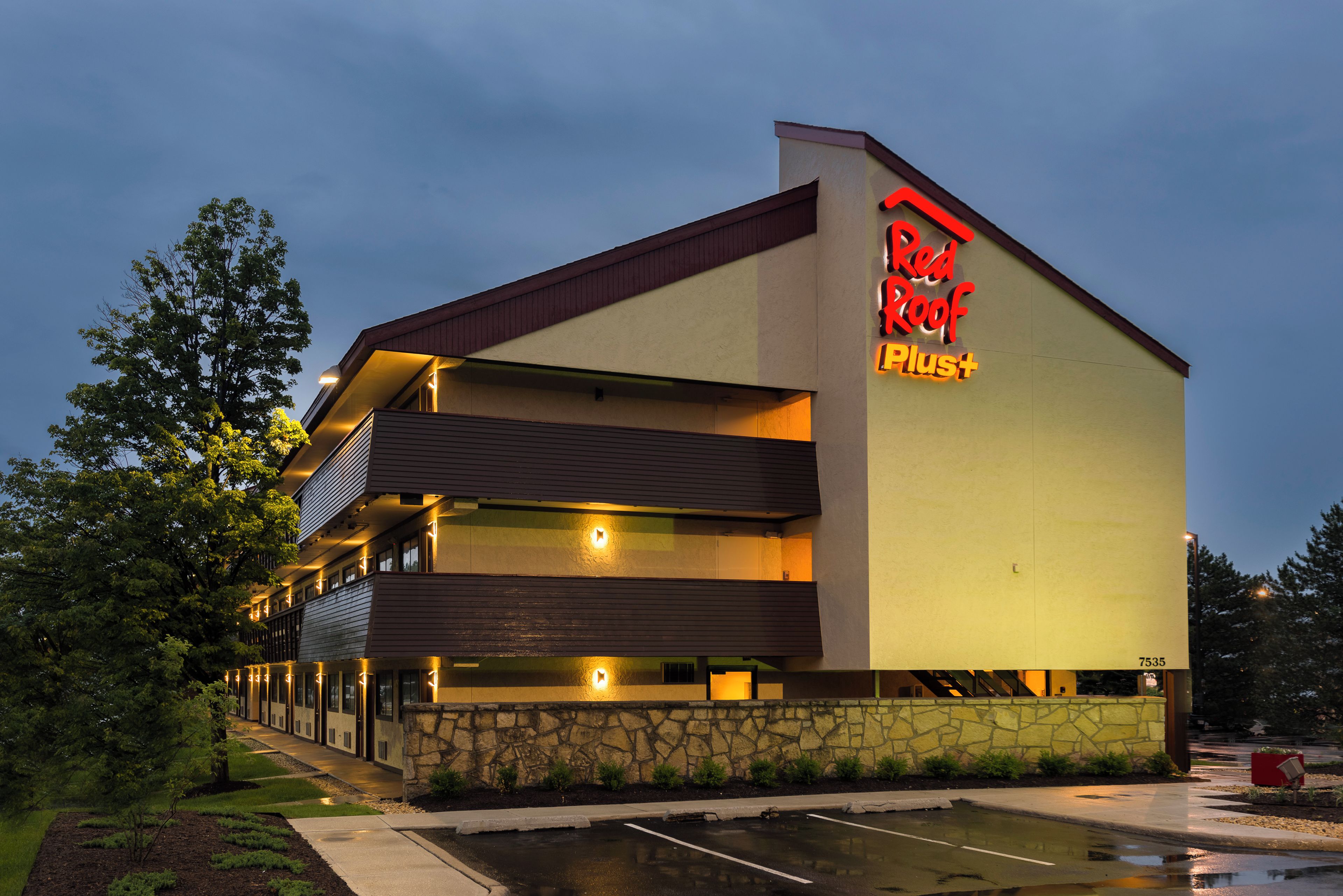 A Red Roof Plus hotel with a two-story structure, a stone facade, and a parking lot.