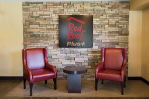 A Red Roof Plus lounge area with two leather chairs and a small table against a stone wall.