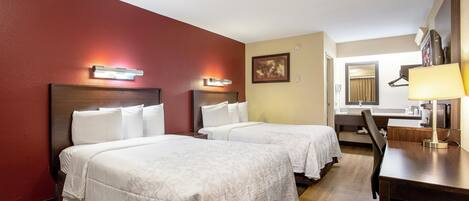 A hotel room with two beds, a desk, a chair, a mirror, and a picture on the wall.