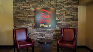 A Red Roof Plus sign on a stone wall with two leather chairs and a small table.