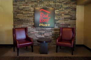 A Red Roof Plus sign on a stone wall with two leather chairs and a small table.