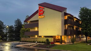 A multi-story hotel with a prominent 'Red Roof Plus' sign, a stone facade, and a landscaped front yard.