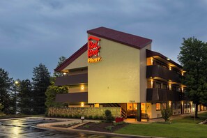A multi-story hotel with a prominent 'Red Roof Plus' sign, a stone facade, and a landscaped front yard.