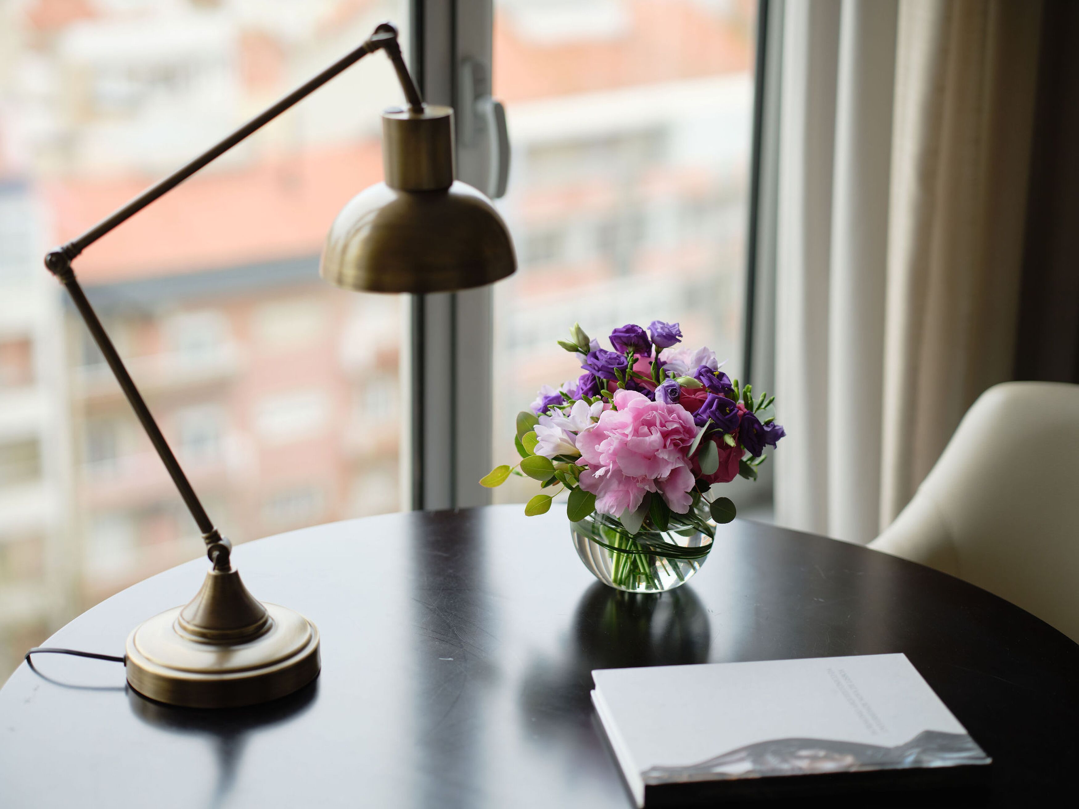 Un bureau avec une lampe, un vase de fleurs et un livre.